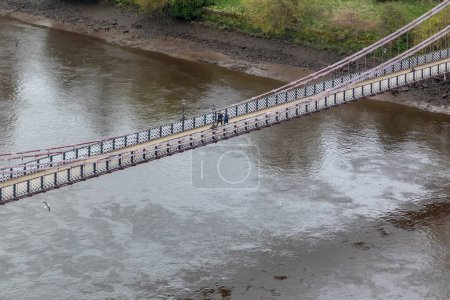 South Portland St Suspension Bridge over the river Clyde in the city of Glasgow, Scotland. Few walking persons and historic town houses on the river bank. High quality photo