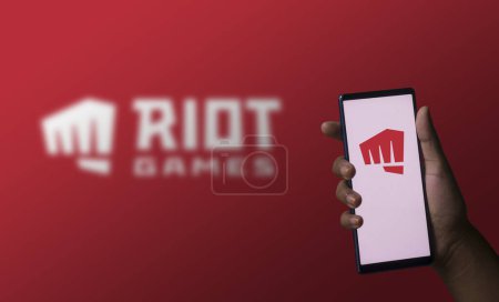Foto de Dhaka, Bangladesh 07 de diciembre de 2023: Una mano sosteniendo un teléfono con el logotipo de los juegos Riot en la pantalla. - Imagen libre de derechos