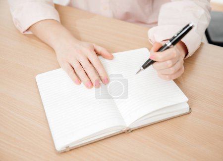 Téléchargez les photos : Close up of a woman's hands writing in a notepad placed on a wooden table, home office and work concept, plans and forecasts, left-handed - en image libre de droit