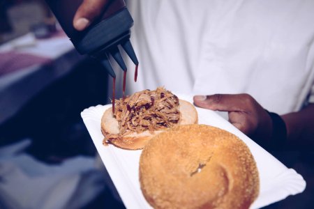 Photo for Hand pouring sauce on pulled pork on a sesame bun - Royalty Free Image