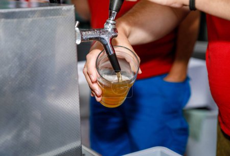 Bière coulant d'un robinet dans un verre transparent tenu par une personne