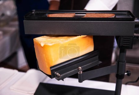 Goldener Raclette-Käse schmilzt auf einem elektrischen Grillgerät