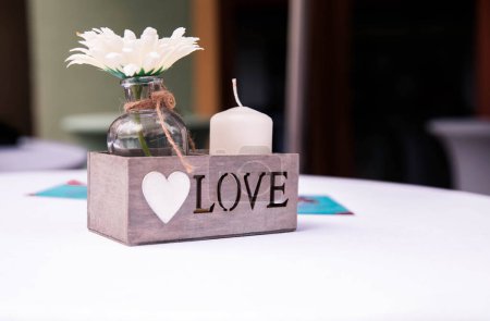 A wooden box with the word LOVE and a candle, on a white table