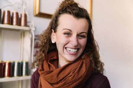 Fröhliche Frau mit lockigem Haar und rostfarbenem Schal in einem Craft Shop, Store-Konzept