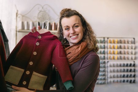 Happy woman with curly hair showcasing a fashionable red and tan jacket, standing in a boutique