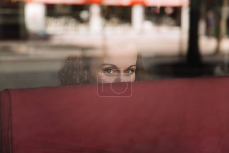 Nachdenkliche Frau blickt hinter einem spiegelnden Glasfenster in einer Großstadt hervor