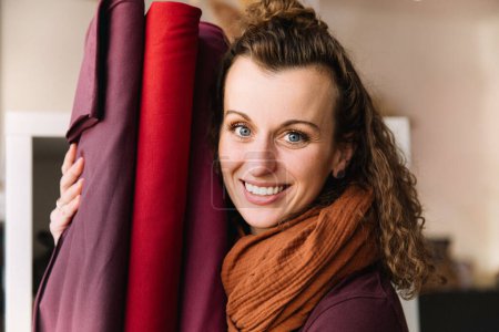 Delighted woman with curly hair bursting into laughter, holding vibrant fabric rolls