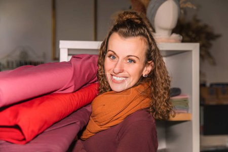 Mujer abrazando una pila de rollos de tela, mostrando entusiasmo en una tienda creativa