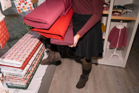 Détail en gros plan des mains d'une femme tenant soigneusement une pile de rouleaux de tissu coloré dans un atelier créatif dynamique et organisé
