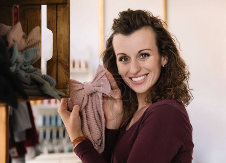 A cheerful fashion designer holding a delicate handmade textile bow, exemplifying her craftsmanship and creative spirit in a well-lit workshop setting