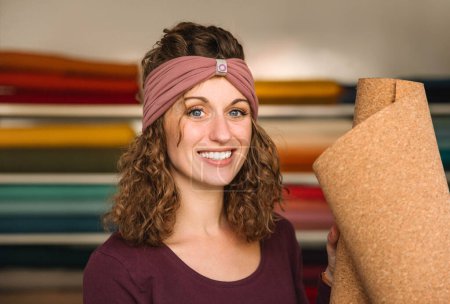 Alegre diseñadora sostiene una hoja de corcho, su expresión alegre que refleja su pasión por los materiales sostenibles en su espacio de trabajo rico en textiles