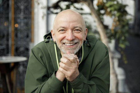 Senior Man with Beard Joyfully Clasping Hands in Green Jacket Outdoors