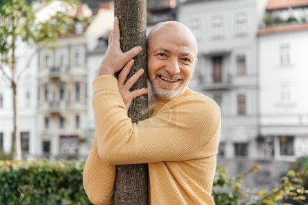 Joyful Senior Man Hugging Tree in Urban Park with Historical Buildings