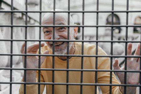 Elderly man showing a vivacious expression while playfully interacting with a metal fence, bringing a lively energy to the urban scene