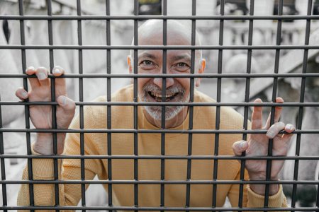 Smiling elderly man with a joyful expression seen through metal bars in a city environment