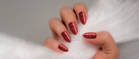 Foto de Female hand with red glitter nails is holding white fur on gray background - Imagen libre de derechos