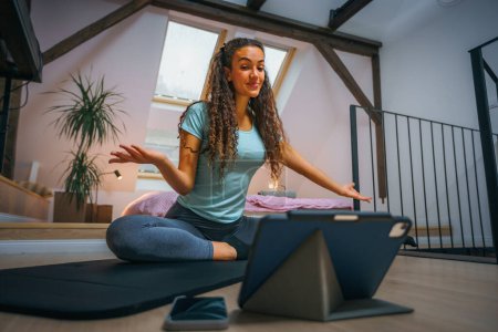 Photo for Fitness coach teaching yoga online to people on her tablet - Royalty Free Image