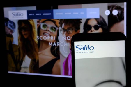 Téléchargez les photos : Au premier plan, le logo spa Safilo Group vu à travers un smartphone et en arrière-plan une page du site de la société cotée à la Bourse de Milan. - en image libre de droit
