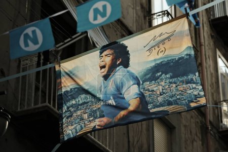 Foto de Banner con la imagen de Diego Armando Maradona vistiendo la legendaria camiseta de fútbol Napoli y el estadio dedicado a él en el fondo. Estamos en los barrios españoles de Nápoles. Celebraciones por Napoli SSC Campeón de Italia 2022 / 23. - Imagen libre de derechos