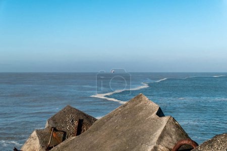 Téléchargez les photos : Quelques rochers sur la digue de Praia do Digue à Boucau avec la mer un peu agitée et un bateau en arrière-plan - en image libre de droit
