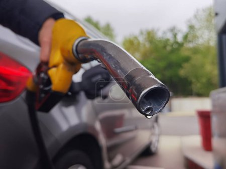 Person mit Benzinpumpe in der Hand nach dem Betanken des Autos