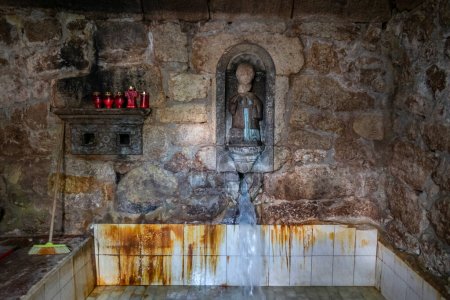 Téléchargez les photos : Cuve en pierre au SPA de Sao Lourenco avec de l'eau sulfureuse qui coule toujours et avec l'image de Sao Lourenco sur le mur - en image libre de droit