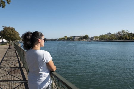 Foto de Mujer frente al río Adour con parte de la ciudad de Bayona al fondo en el País Vasco - Imagen libre de derechos