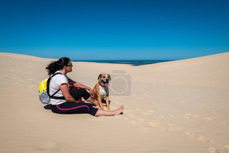 Téléchargez les photos : Touriste assise avec son chien sur les Dunes du Pilat en France - en image libre de droit