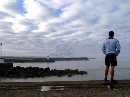 Téléchargez les photos : Jeune touriste face à la mer, avec quelques jours d'avance par une journée d'hiver nuageuse et brumeuse - en image libre de droit