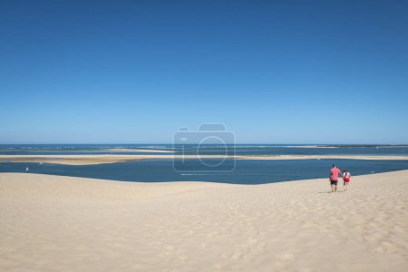 Téléchargez les photos : Quelques touristes marchant dans les dunes du Pilat par une chaude journée avec un ciel bleu - en image libre de droit
