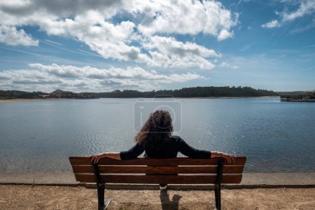Photo for Tourist woman sitting relaxing on a garden bench in front of the lake in Vieux Boucau les Bains in the French Basque Country - Royalty Free Image