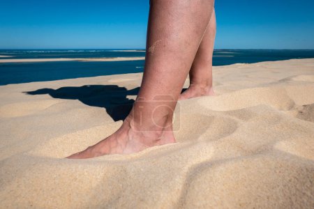 Téléchargez les photos : Jambe du touriste sur le sable tout en se reposant et bronzant - en image libre de droit