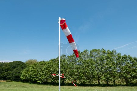 Photo for Rotating cone that indicates the direction of the wind placed on a landing site for skydiving in the middle of some trees and green grass - Royalty Free Image
