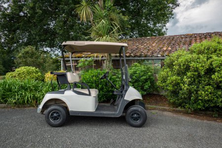 Téléchargez les photos : Chariot de golf garé sur le bord de la route pour la pratique du sport de golf par une journée très nuageuse - en image libre de droit