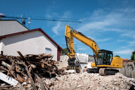 Téléchargez les photos : Pelle rétrocaveuse démolir une vieille maison pour une construction ultérieure sur le site - en image libre de droit