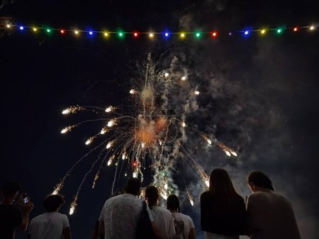 Foto de Coloridos fuegos artificiales en el cielo nocturno con algunas personas viendo el evento festivo - Imagen libre de derechos