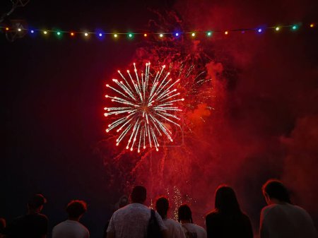 Foto de Coloridos fuegos artificiales en el cielo nocturno con algunas personas viendo el evento festivo - Imagen libre de derechos