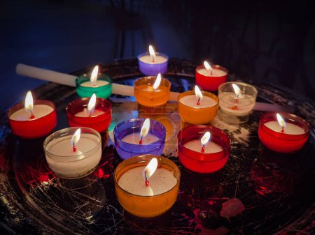 Téléchargez les photos : Quelques bougies de différentes couleurs brûlant à l'intérieur sombre d'une église - en image libre de droit