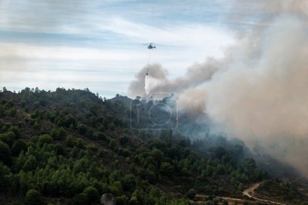 Foto de El poder del agua: el helicóptero se enfrenta a las llamas de la destrucción que deja mucho humo en el aire - Imagen libre de derechos