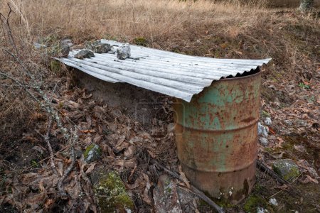 Foto de Un tambor viejo con una placa de zinc en la parte superior para usar agua de lluvia para riego posterior - Imagen libre de derechos