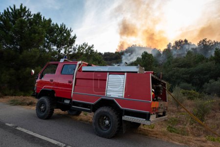 Foto de Camión de bomberos junto a una carretera que lucha contra un incendio forestal con grandes llamas que dejan una gran nube de humo en el aire - Imagen libre de derechos