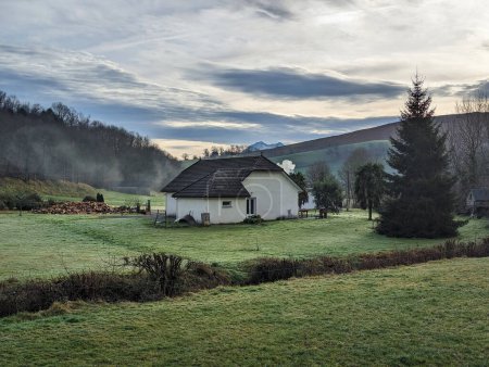 Téléchargez les photos : Ferme rurale avec des pâturages verts et une forêt avec une maison au milieu d'une journée avec un ciel spectaculaire - en image libre de droit