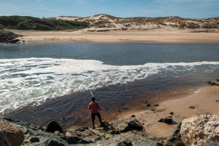 Téléchargez les photos : Tranquillité au bord de la mer : pêcheur contemplatif avec sa canne à pêche, entouré de rochers, au Pays basque français - en image libre de droit