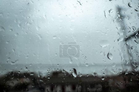 Regentropfen am Fenster: Ein verschwommener Blick auf die Stadt durch den nassen grauen Glashintergrund