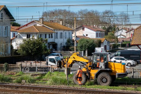 Workers performing maintenance on train lines with a front-loading machine in the middle of an urban area