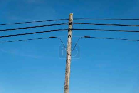 Wooden pole supporting telephone cables against a blue sky