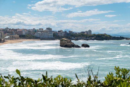 Part of the city of Biarritz by the sea with some rocks on the beach on a partly cloudy day with some waves