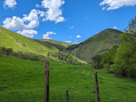 Frühling in den Bergen mit grünen Weiden, umgeben von einem Holzzaun und einem Himmel mit kleinen Wolken