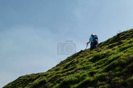 Touristin wandert an einem sonnigen Tag mit Stöcken in der Hand auf einem Berg mit steilem Hang