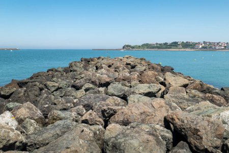 Téléchargez les photos : Fortification avec des pierres dans la mer de Saint Jean de Luz, avec une partie de la ville en arrière-plan au Pays Basque en France - en image libre de droit
